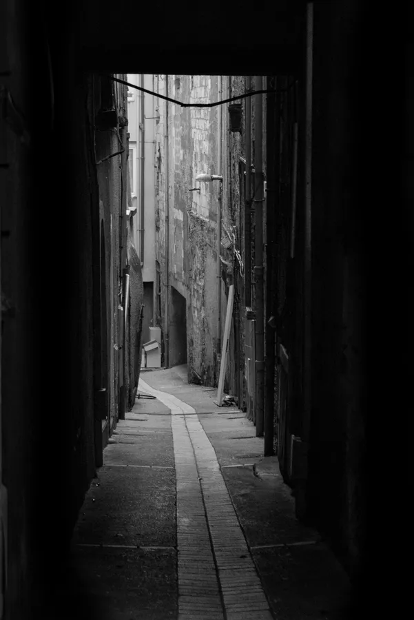 Ruelle étroite en noir et blanc entre de hauts murs anciens.