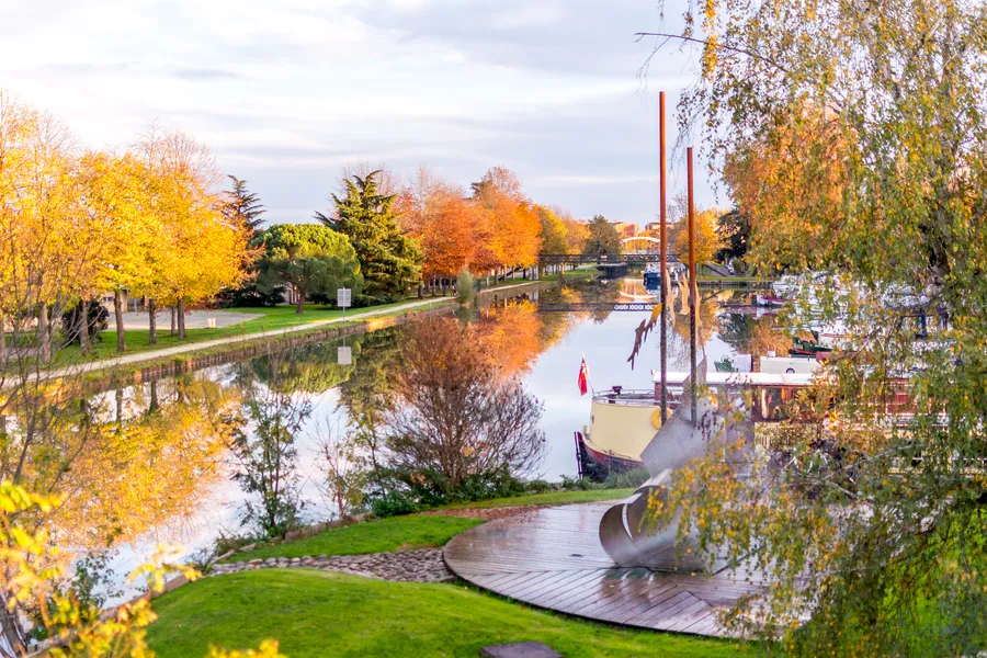 Paysage de canal aux couleurs d’automne avec bateaux et reflets.