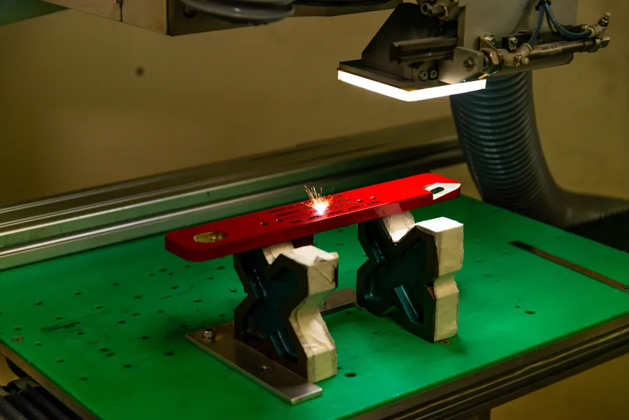 Machine laser travaillant une pièce métallique rouge.