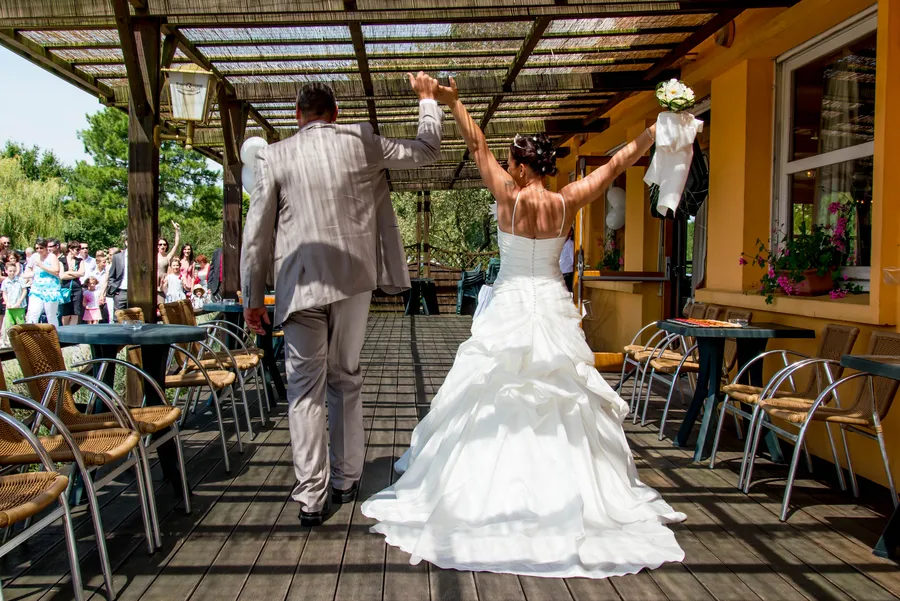 Couple de mariés s’éloignant en levant les bras.
