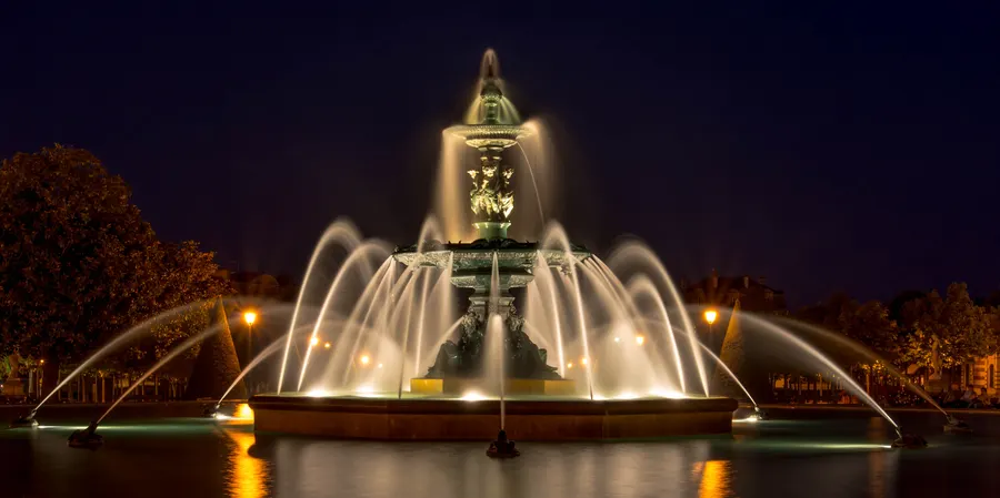 Fontaine illuminée de nuit devant une tour.