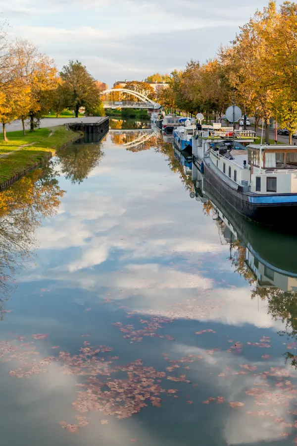 Canal bordé d’arbres d’automne et de bateaux amarrés.