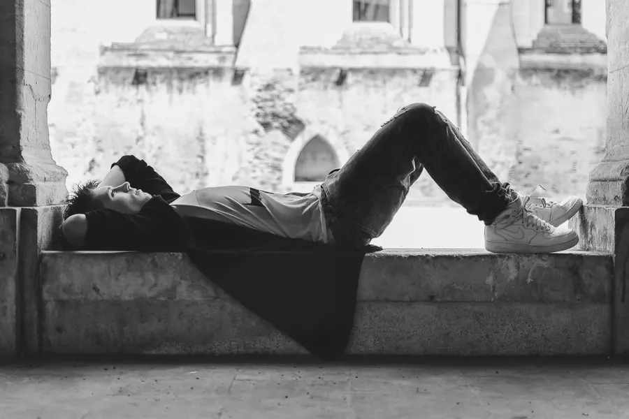 Portrait en noir et blanc d’une personne allongée dans un bâtiment ancien.