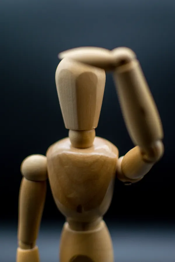 Mannequin articulé en bois portant la main au front.