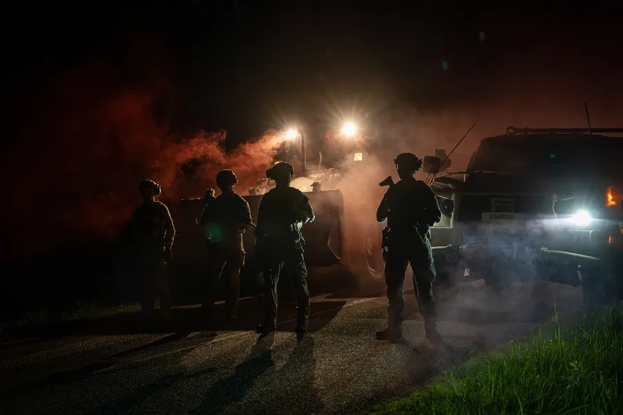 Silhouettes de nuit éclairées par des véhicules et de la fumée.