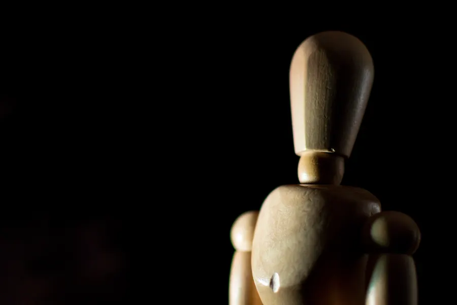 Mannequin articulé en bois éclairé latéralement sur fond sombre.