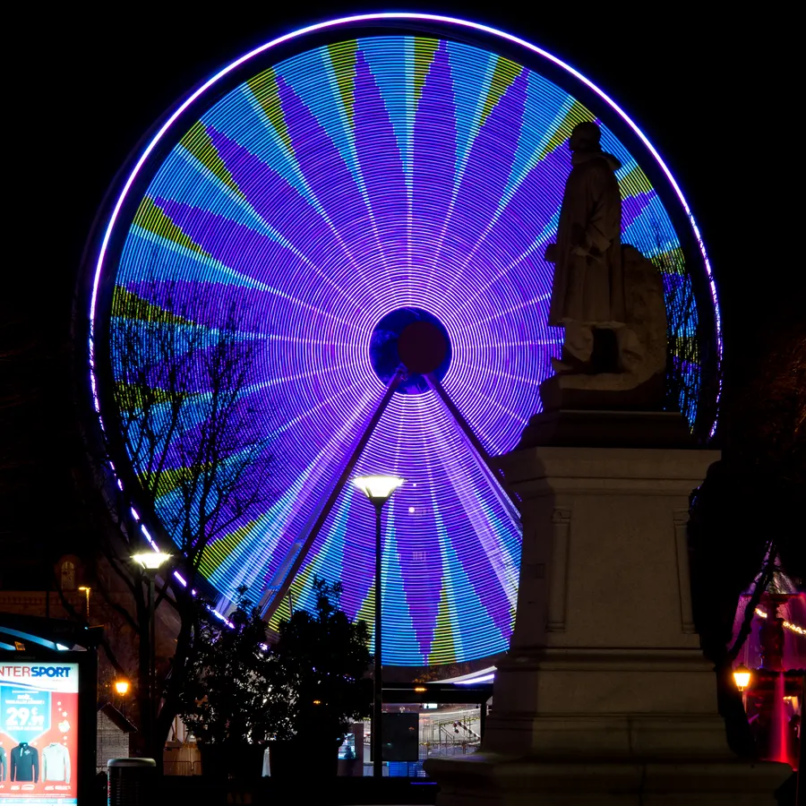 Grande roue illuminée de nuit derrière une statue.