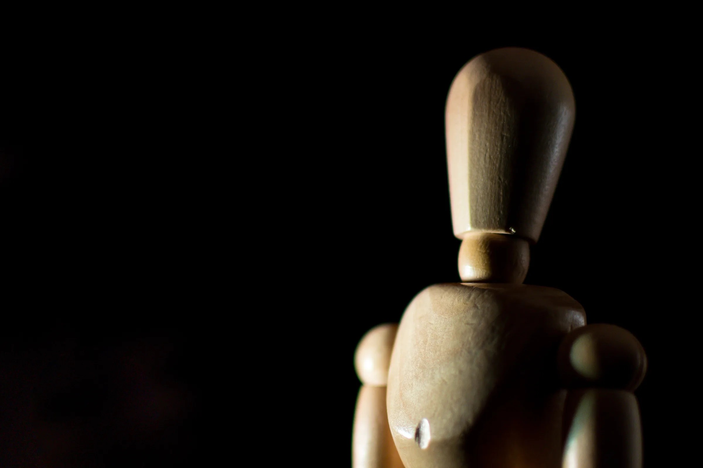 Mannequin articulé en bois éclairé latéralement sur fond sombre.